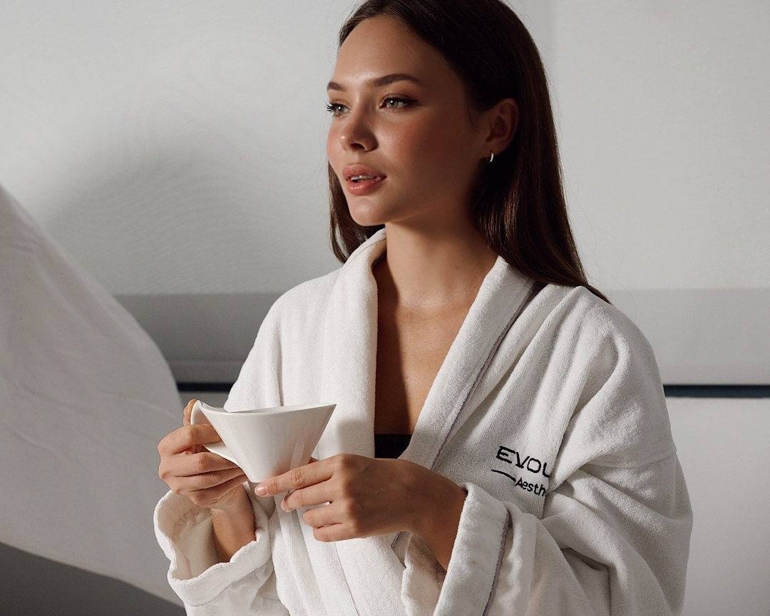 Woman in an Evolution Aesthetics robe holding a cup in a wellness setting