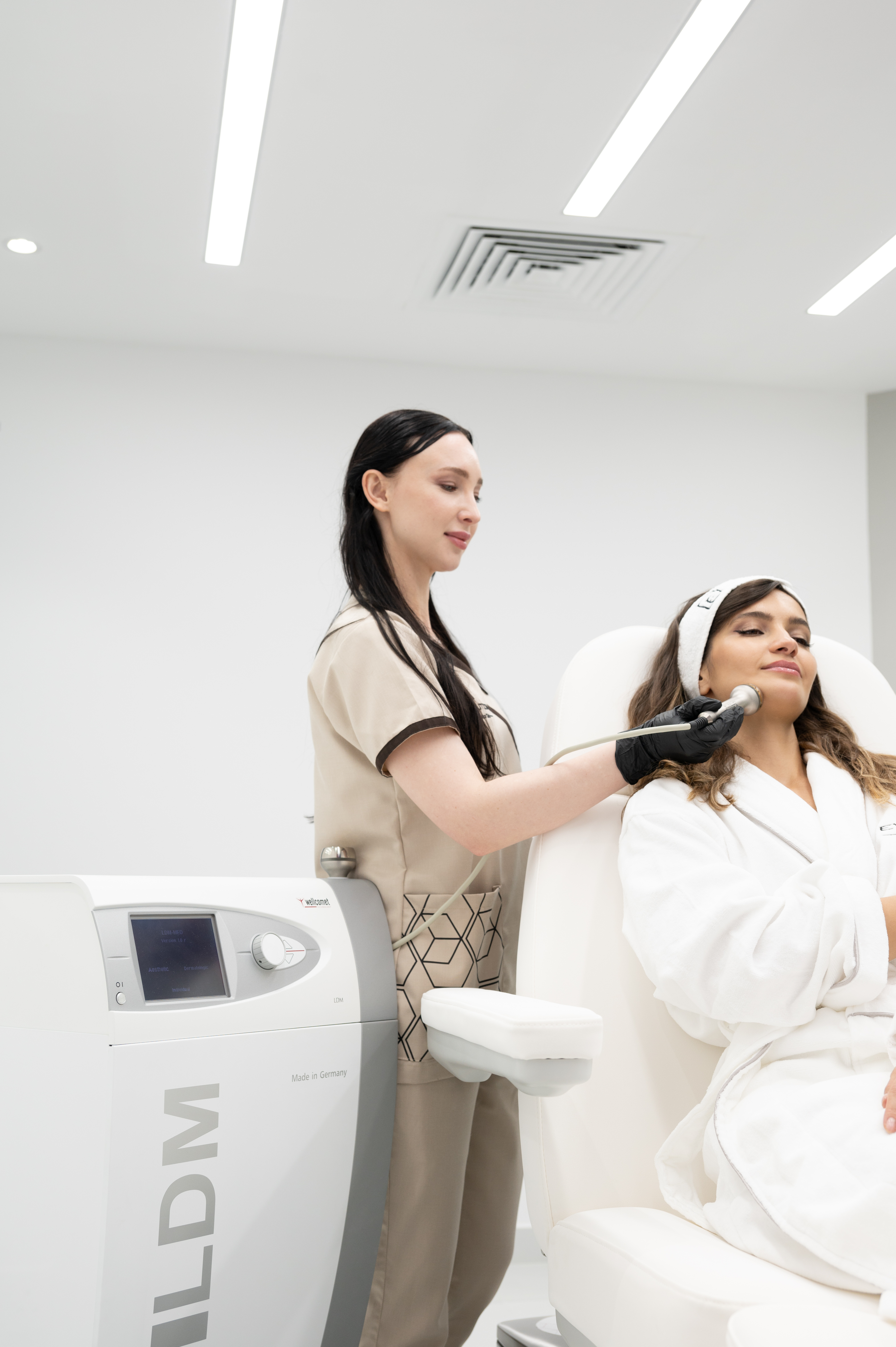 Practitioner providing a facial LDM treatment with the device beside the patient