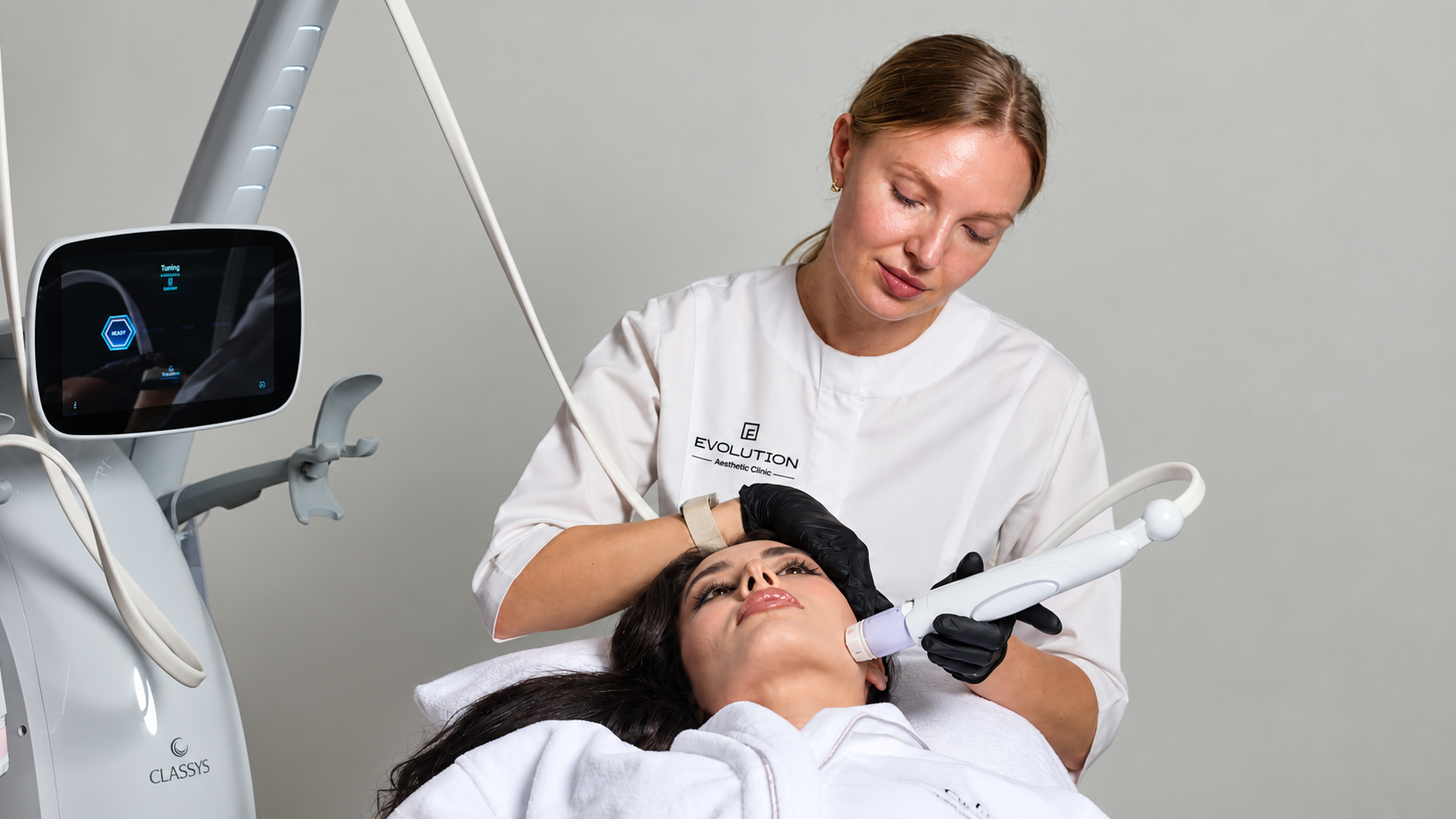 Clinician applying a Volnewmer handpiece to a patient’s jaw, with the treatment device beside the bed at Evolution Aesthetics Clinic.
