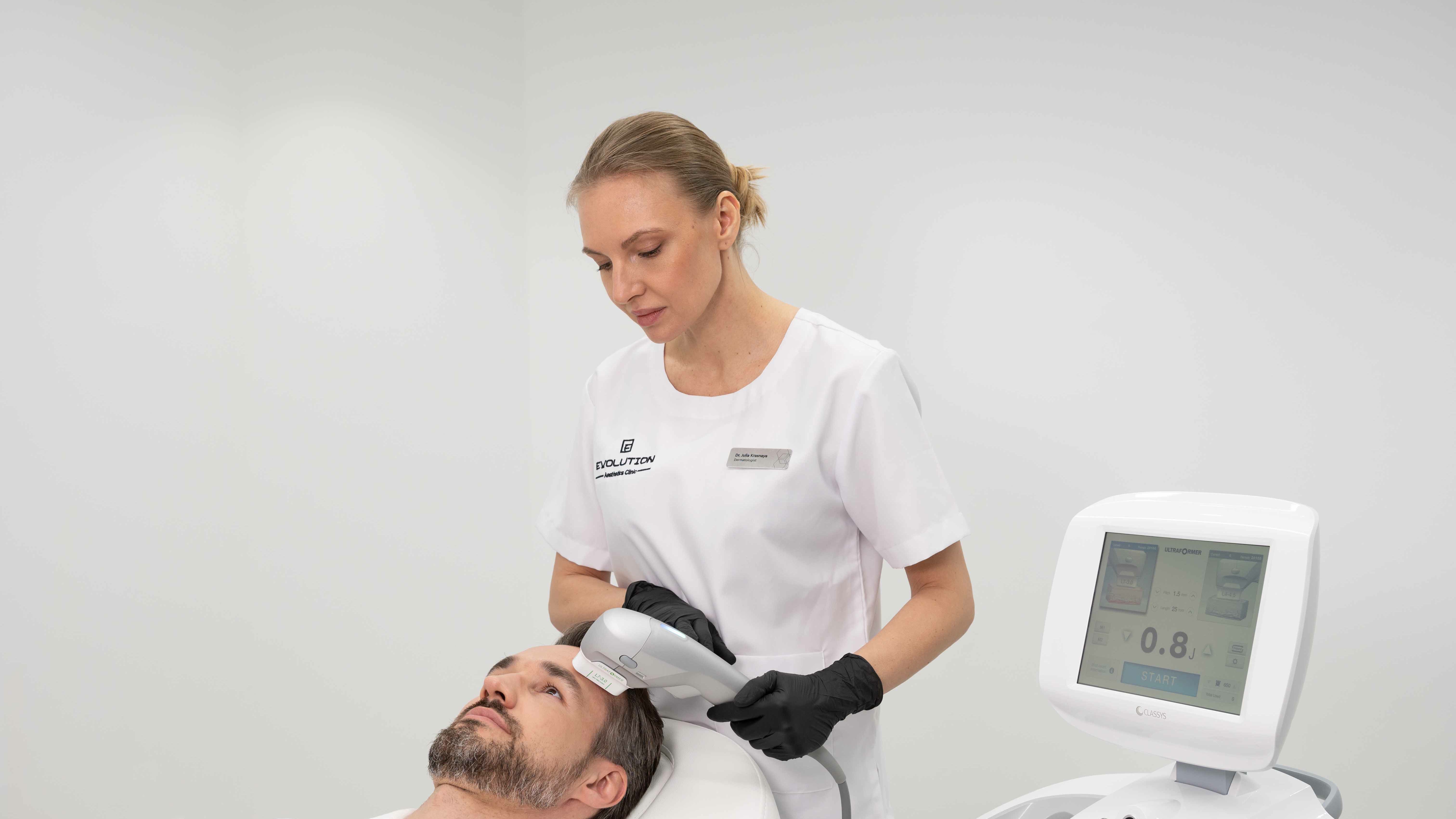 Ultraformer handpiece applied to a patient's forehead beside the treatment console