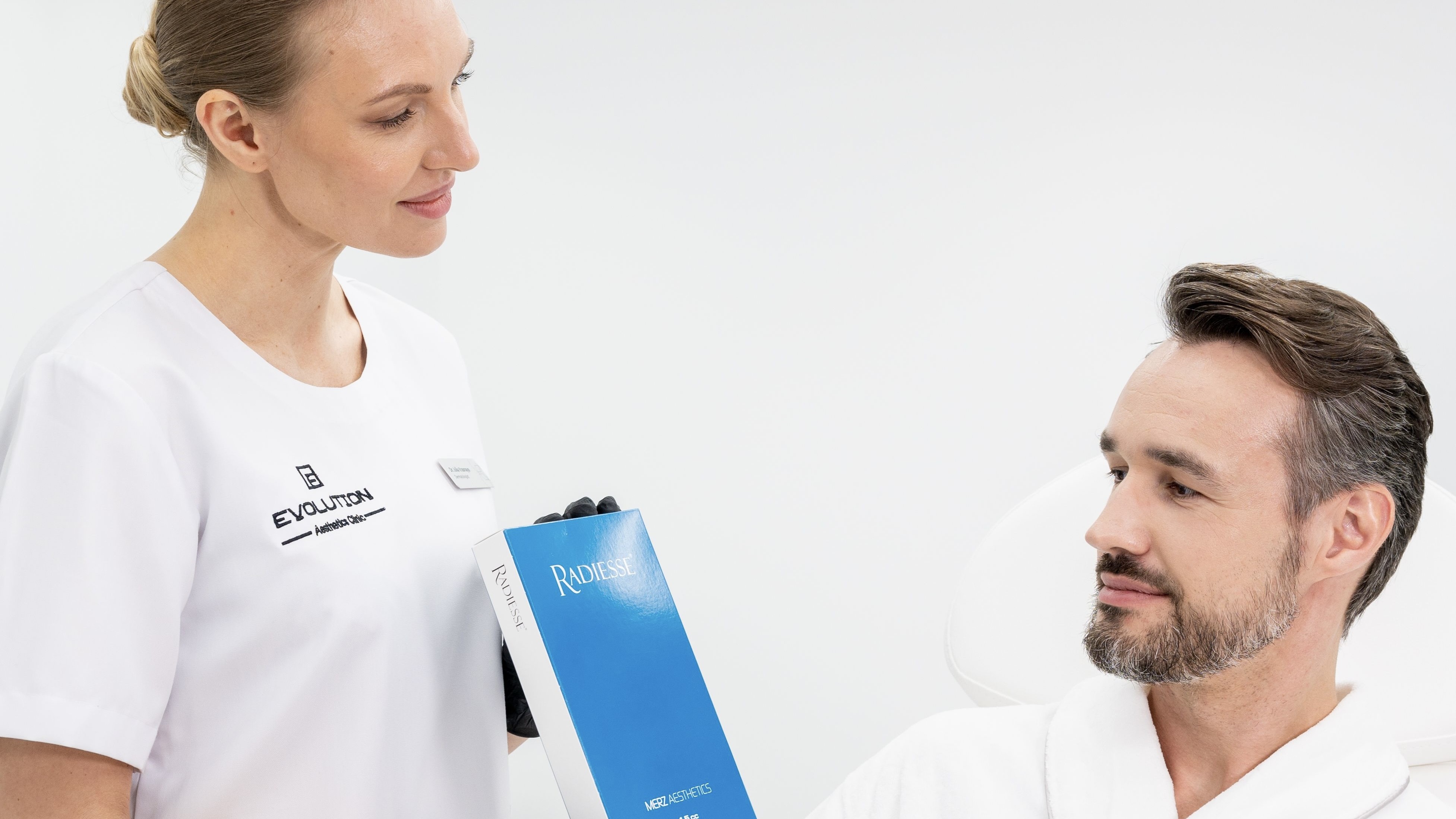 Only catalog scene that pairs the actual Radiesse product with a real patient in a two-person consultation; landscape source, both faces survive the crop